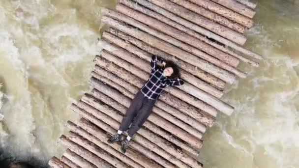 Молодая женщина лежит с руками под головой на речном мосту — стоковое видео