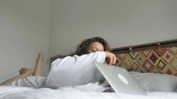 Happy woman falls on bed opens laptop smiling and types — Stock Video