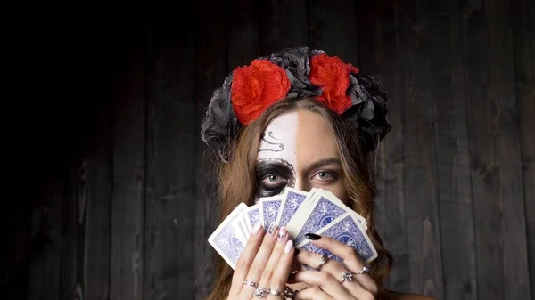 Lady model z makijażem czaszki pokazuje karty pod drewnianą ścianą — Zdjęcie stockowe
