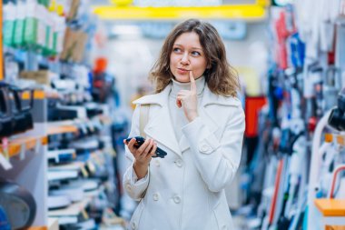 Kadın, elinde telefonla bir süpermarkette ev aletleri satan bir mağazadan satın almayı düşündü.