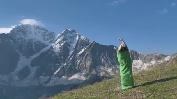 Une personne dans un sac de couchage vert saute et agite les mains — Video