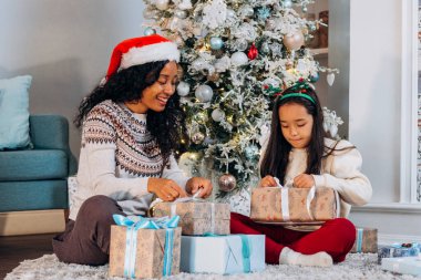 Anne ve kızı halıya oturup Noel hediyelerini açarlar.