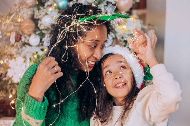 Siyah anne ve kız, çelenge sarılmış şekilde poz veriyorlar.