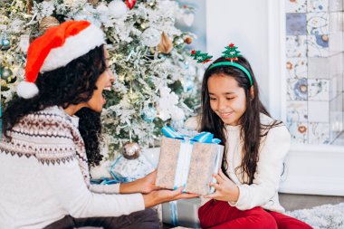 Anne ve kızı halıya oturup Noel hediyelerini açarlar.