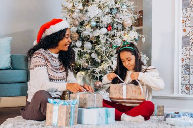 Anne ve kızı halıya oturup Noel hediyelerini açarlar.