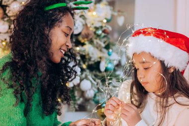 Siyah anne ve kız, çelenge sarılmış şekilde poz veriyorlar.