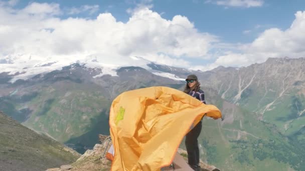 Lady tourist in cap fastens tent on hillside rocky ground — Stock Video