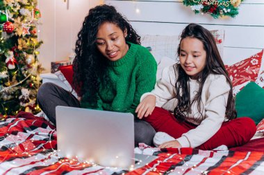 Kız ve siyah anne yatakta dizüstü bilgisayarla iletişim kuruyor.