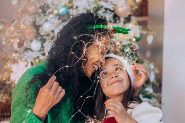 Siyah anne ve kız, çelenge sarılmış şekilde poz veriyorlar.