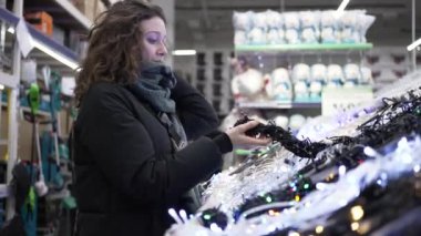 Süpermarkette genç bir kadın Noel çelengi seçiyor.