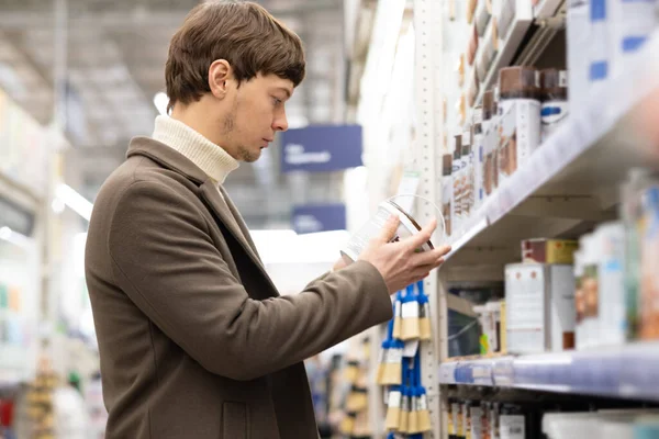 European man holding a can of paint in his hands at a hardware store, renovating a house — Stock Photo, Image