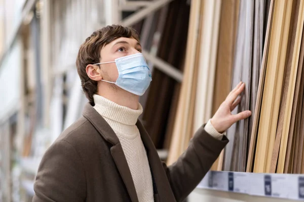 Een man in een bruine jas en een beschermmasker kiest voor houten materialen in een bouwsupermarkt — Stockfoto