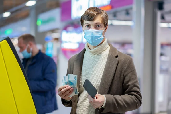 Een jonge man met een medisch masker nam 3000 roebel van een geldautomaat in een winkelcentrum. — Stockfoto