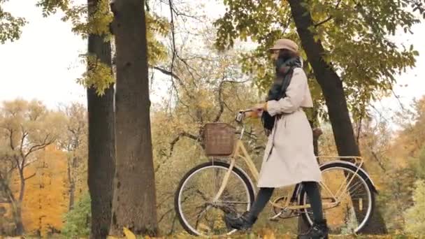 Młoda kobieta spaceruje z rowerem przeciwko żółtym drzewom w parku — Wideo stockowe