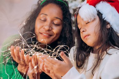 Siyah anne ve kız, çelenge sarılmış şekilde poz veriyorlar.