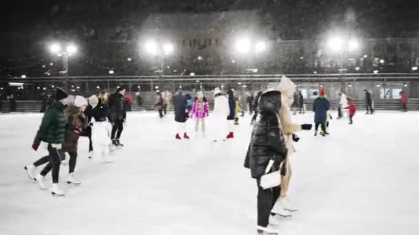 Mensen rijden 's avonds op een ijsbaan tijdens een sneeuwval — Stockvideo