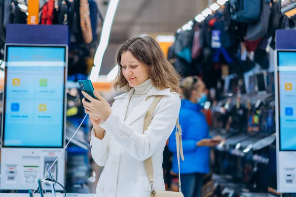 Женщина с длинными вьющимися волосами выбирает новый телефон в магазине — стоковое фото