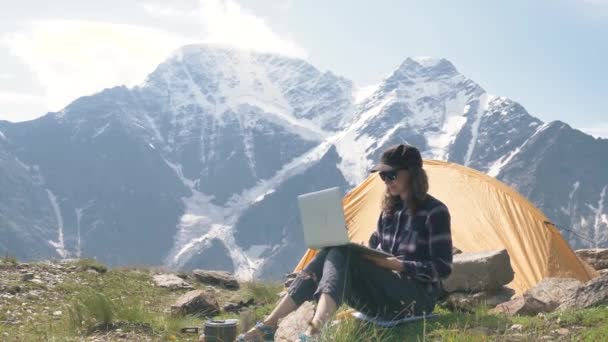 Señora se sienta en la cima de la colina y los tipos en el ordenador portátil contra las montañas — Vídeo de stock