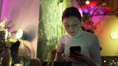 Genç bir kadın kafeteryada yemek yerken sosyal medyada geziniyor.