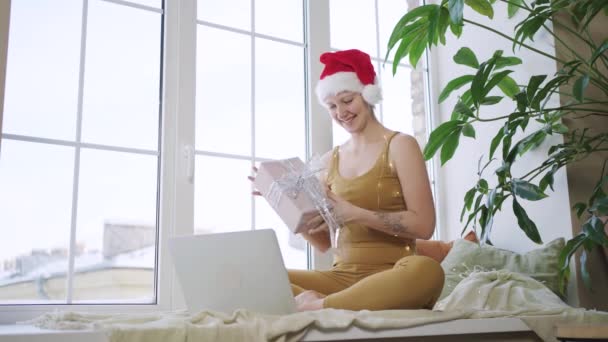 Woman in Santa hat unwraps present box showing to laptop — Stock Video
