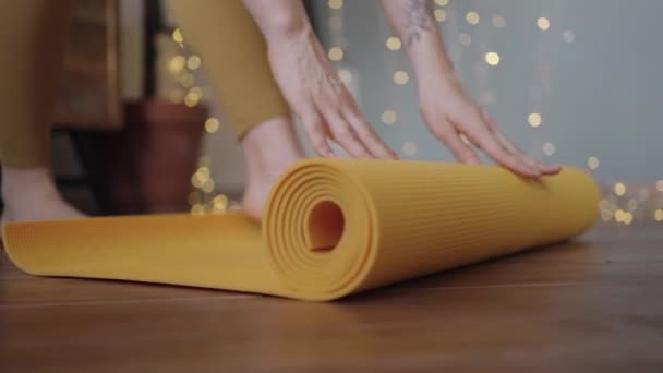 Mujer joven desenrolla alfombra de yoga amarillo antes de practicar — Vídeo de stock