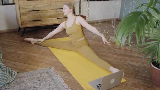 Woman with blonde hair does yoga on mat watching tutorial — Stock Video