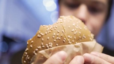 Aç ve iştahlı bir adam hamburgeri yakından yiyor.