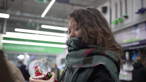 Cute woman chooses christmas glass ball with sparkles in supermarket — Stockvideo