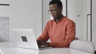 African-American guy works on laptop sitting at white table