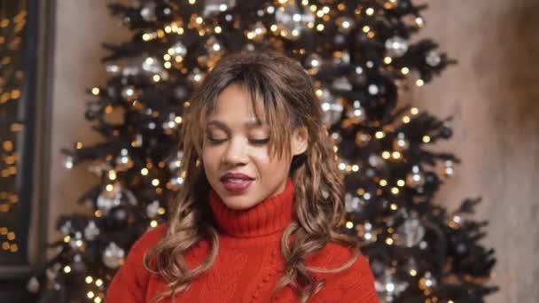 Young woman opens present sitting against Christmas tree — Vídeo de stock