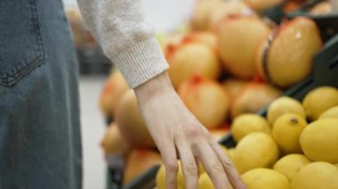 Woman walks along containers with lemons and picks apples