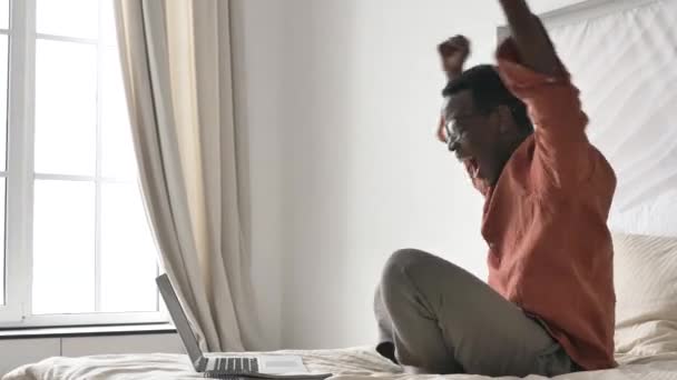 Funny African-American man screams with joy at modern laptop — стоковое видео