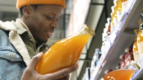 African-American man carefully reads the composition of the juice in the supermarket and selects the product, puts it in the shopping cart — Video Stock