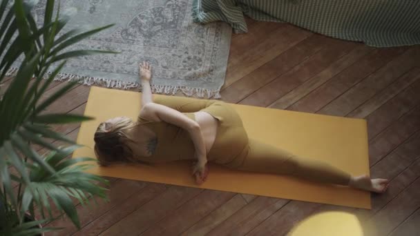 Mujer joven rubia delgada hace yoga en la estera tumbada en el suelo — Vídeos de Stock