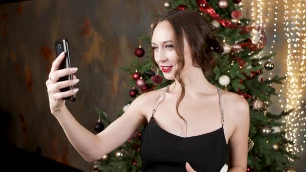 Woman with hairstyle talks via videocall near Christmas tree — Vídeo de stock
