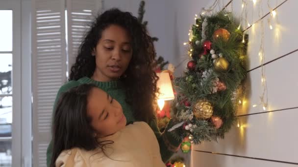 Daughter and African American mom decorate wall with Christmas wreath — Vídeo de stock