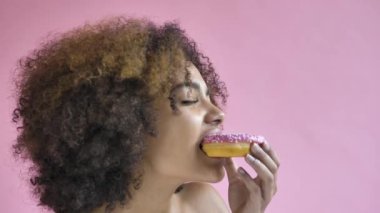 Curly haired young woman model bites delicious doughnut