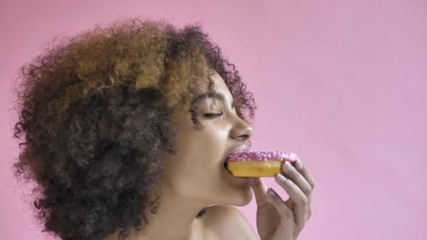 Curly haired young woman model bites delicious doughnut — 图库视频影像