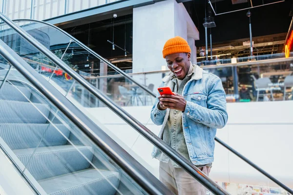 Щасливий афро-американець дивиться на телефонний зв'язок вгору ескалатор — стокове фото