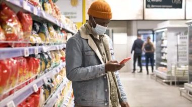 Black guy in yellow hat and denim jacket types on smartphone