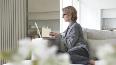 Concentrated short haired blonde young woman types on laptop