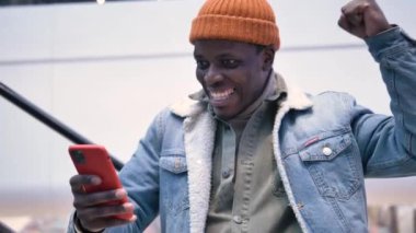 Amazed black shopaholic in hat raises hand with happiness