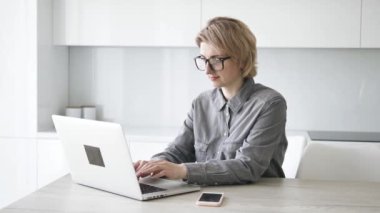 Short haired businesswoman types on white laptop at table