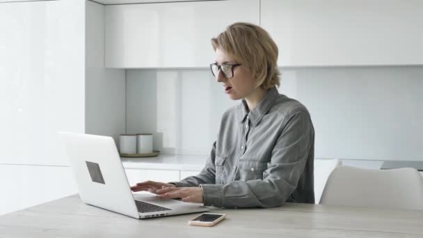 Blonde lady freelancer in grey shirt types on white laptop — Stockvideo
