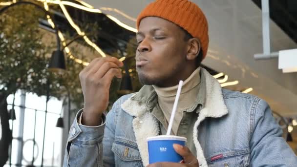 Black guy in blue denim jacket eats delicious chips in cafe — Vídeo de Stock