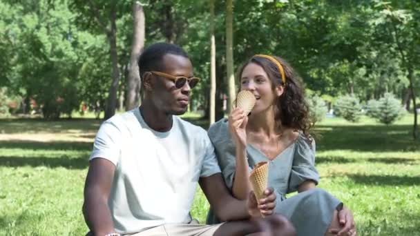 Black man and brunette eat organic ice-cream on grass lawn — Vídeos de Stock