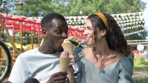 Black man and brunette eat organic ice-cream on grass lawn — Vídeos de Stock