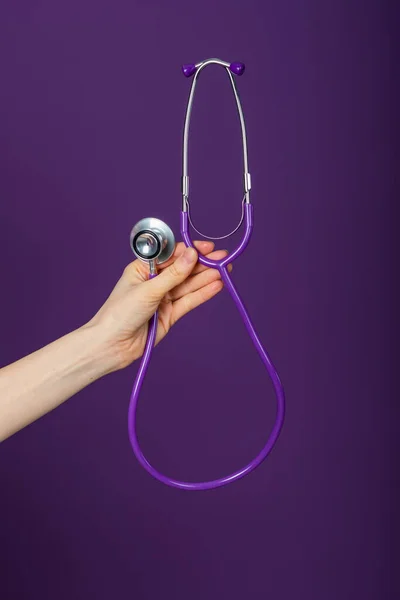 Doctors hand holding a purple stethoscope on a purple background