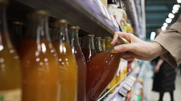 Mujer busca jugo fresco tomando botella de vidrio de estante — Foto de Stock