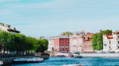 Touristic boats sail on long river with blue water running past vintage buildings. Old city with beautiful architecture and lush trees time lapse. The city center of St. Petersburg, Fontanka river.